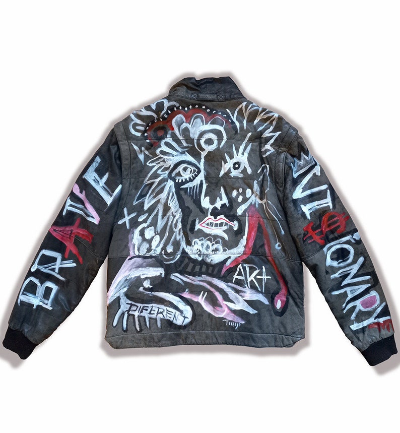 Puede incluir: Chaqueta de cuero negra con un dise&ntilde;o pintado a mano que presenta una cara, formas abstractas y las palabras "Brave", "Art", "Different" y "Revolutionary".