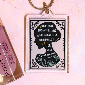 May include: A clear acrylic keychain featuring a black and white silhouette of a woman's head. The text on the keychain reads "Her own thoughts and reflections were habitually her best companions. Jane Austen."