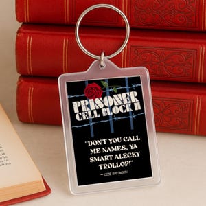 May include: A clear rectangular keychain with a silver ring. The keychain features the text "PRISONER CELL BLOCK H" with a rose and barbed wire design. Below the text is the quote, "DON'T YOU CALL ME NAMES, YA SMART ALECKY TROLLOP!" by Lizzie Birdsworth.