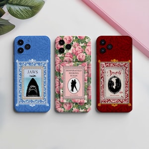 May include: Three phone cases with book cover designs. The blue case features a "JAWS" movie poster. The floral case has "Desperately Seeking Susan". The red case displays "Dracula".