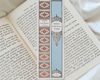 May include: A decorative bookmark featuring a light blue background with ornate white and pink accents. The bookmark has text that reads "Lyrics of the Heart" and "Byron's Poetical Works" in elegant fonts. The bookmark is resting on the pages of an open book.