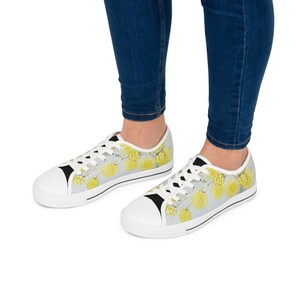 May include: White canvas low-top sneakers with a floral print featuring yellow flowers and green leaves.