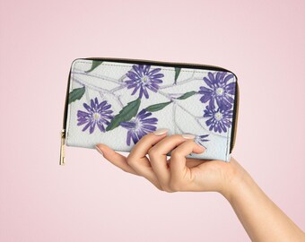 Op de afbeelding: Een witte portemonnee met rits met een bloemenprint met paarse bloemen en groene bladeren.