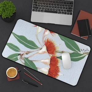 Puede incluir: Alfombrilla de ratón rectangular con una pintura de acuarela de flores rojas y blancas y hojas verdes sobre un fondo azul claro. Un ratón de ordenador blanco está sobre la alfombrilla, con un portátil, cuadernos y una taza de café cerca.