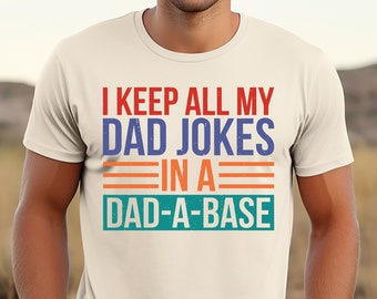 Op de afbeelding: Een wit T-shirt met een blauwe, rode en oranje afbeelding met de tekst "Ik bewaar al mijn vadersmoppen in een vadersmoppen-database".