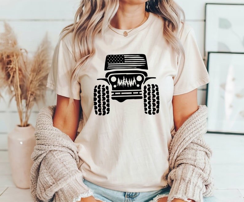 Puede incluir: Una camiseta blanca con una silueta negra de un Jeep con una bandera americana en el cap&oacute;. El Jeep tiene neum&aacute;ticos negros y una parrilla negra.