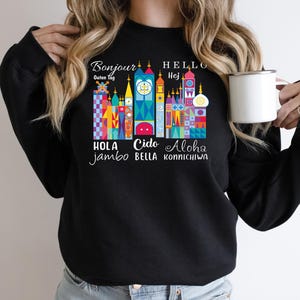 May include: Black sweatshirt with a colorful graphic of a castle with text in multiple languages, including "Bonjour", "Hello", "Hola", "Cido", and "Aloha".