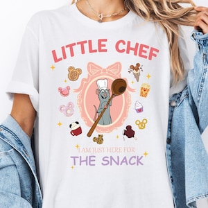 Może przedstawiać: Biała koszulka z różową i białą ilustracją szczura szefa kuchni trzymającego drewniany łyżkę. Tekst "Little Chef" znajduje się na górze koszulki, a "I am just here for the snack" na dole.