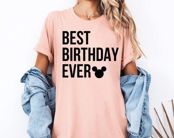 Peut inclure: Un t-shirt rose avec le texte "BEST BIRTHDAY EVER" en lettres noires et une silhouette de Mickey Mouse noire.
