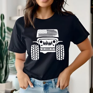 Puede incluir: Una camiseta negra con un gr&aacute;fico blanco de un Jeep con una bandera estadounidense en el cap&oacute;. El Jeep tiene neum&aacute;ticos grandes y una parrilla con un dise&ntilde;o estilizado.