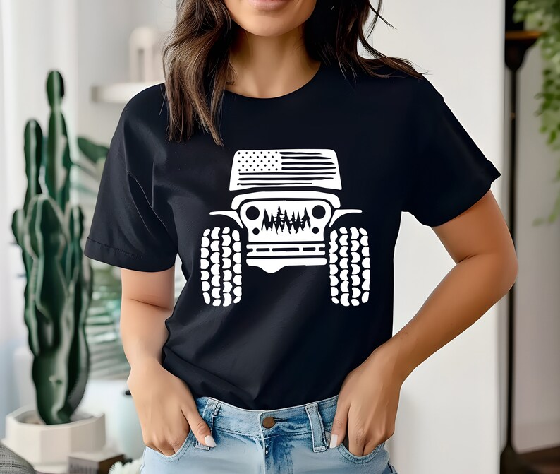 Puede incluir: Una camiseta negra con un gr&aacute;fico blanco de un Jeep con una bandera estadounidense en el cap&oacute;. El Jeep tiene neum&aacute;ticos grandes y una parrilla con un dise&ntilde;o estilizado.