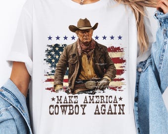 May include: White t-shirt featuring a graphic of a cowboy in a hat and jacket, set against a distressed American flag design. The text "MAKE AMERICA COWBOY AGAIN" is printed below the image.