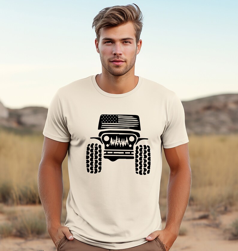 Puede incluir: Una camiseta blanca con una silueta negra de un Jeep con una bandera estadounidense en el cap&oacute;. El Jeep tiene neum&aacute;ticos grandes y una parrilla con una escena de bosque en su interior.
