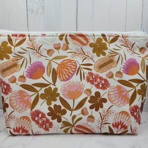 May include: A rectangular make-up bag featuring a floral design in orange, pink, and brown on a white background. The bag has a white zip and is likely made of fabric.