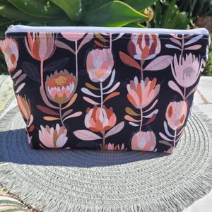 May include: Black zippered pouch with a floral print featuring pink, orange, and gold protea flowers on a black background.