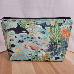 May include: A blue and green zippered pouch with a colourful underwater scene featuring fish, sea turtles, a manatee, an octopus, and a whale.