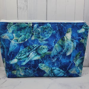 May include: A blue zippered pouch with a white zipper and a repeating pattern of sea turtles on a blue and green background. The text "Stitch & Sew" is visible in the lower right corner.