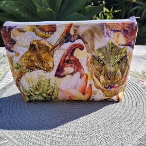 May include: White zippered pouch with a colourful watercolour print of various dinosaurs. The print features a variety of dinosaurs, including a T-Rex, a Triceratops, and a Stegosaurus.