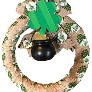 Pode incluir: Uma coroa de juta marrom decorada com fita vichy verde e branca com um padrão repetido de gnomos segurando trevos. Um recorte de trevo verde com uma moeda de ouro e uma panela preta estão presos ao topo da coroa.