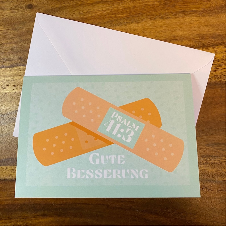 May include: A light blue card with two orange plasters on it. The plasters are crossed over each other. The top plaster has a blue square with the text "PSALM 41:3" on it. The card says "GUTE BESSERUNG" in white text.