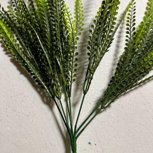 May include: A bundle of artificial greenery with multiple stems. The leaves are a vibrant green, with a slightly lighter shade on the tips. The stems are a darker green, and the overall arrangement is dense and full.