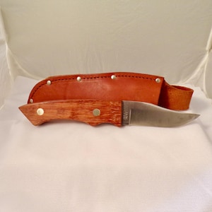 May include: A brown wooden handled knife with a stainless steel blade and a brown leather sheath. The sheath has brass rivets.