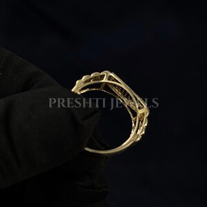 May include: A gold-colored ring with an openwork design. The ring has a delicate, ornate pattern with a series of small, raised elements along the top. The text "PRESHTI JEWELS" is visible on the ring.