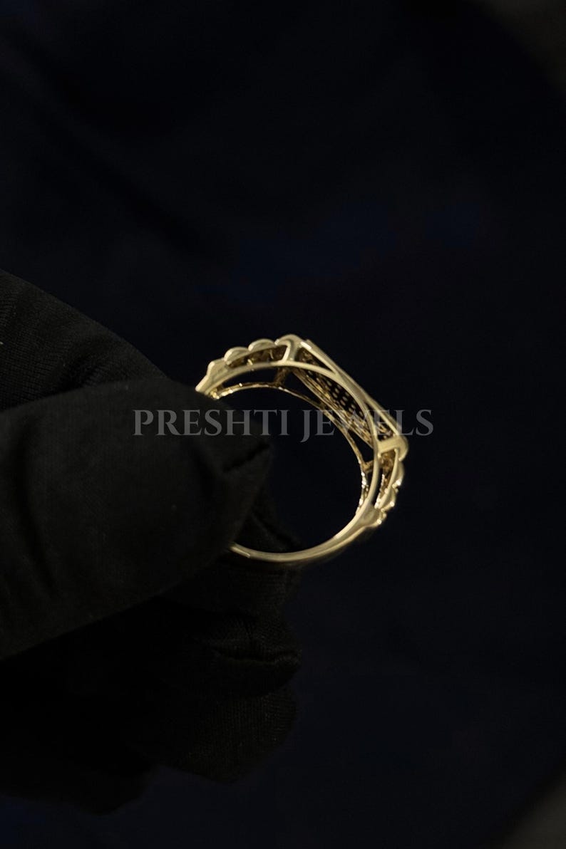 May include: A gold-colored ring with an openwork design. The ring has a delicate, ornate pattern with a series of small, raised elements along the top. The text "PRESHTI JEWELS" is visible on the ring.