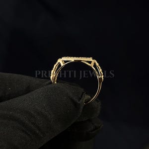 May include: A gold ring with a rectangular center stone, held against a black background. The ring has a delicate design with intricate detailing around the stone and band. The text "PRIHTI JEWLS" is visible.