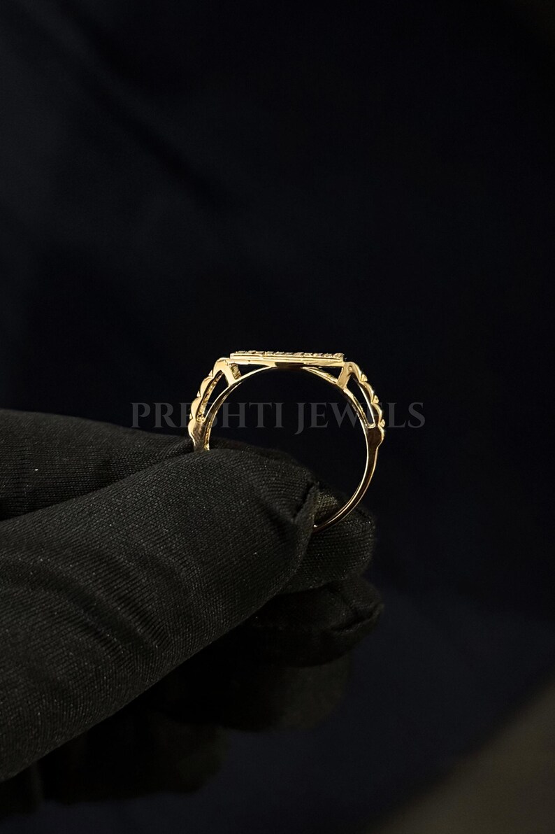 May include: A gold ring with a rectangular center stone, held against a black background. The ring has a delicate design with intricate detailing around the stone and band. The text "PRIHTI JEWLS" is visible.