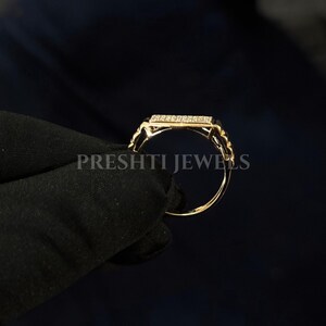 May include: A gold ring with a rectangular top encrusted with small, clear stones. The band has a delicate, rope-like design. The ring is held against a dark background. The text "PRESHTI JEWELS" is visible.