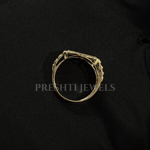 May include: A gold-colored ring with an intricate design. The ring features a rectangular center stone and delicate filigree detailing on the sides. The text "PRESHTI JEWELS" is printed on the black background.