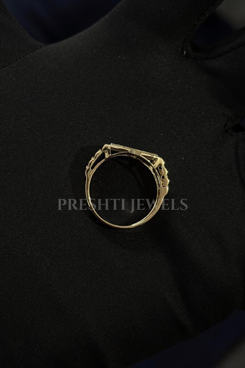 May include: A gold-colored ring with an intricate design. The ring features a rectangular center stone and delicate filigree detailing on the sides. The text "PRESHTI JEWELS" is printed on the black background.