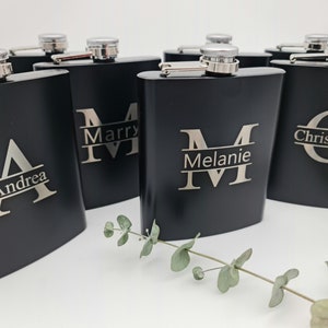 Könnte beinhalten: Ein Set aus sechs schwarzen, personalisierten Flachmännern mit silbernen Schriftzügen. Die Flachmänner sind mit den Namen "Andrea", "Marry", "Melanie" und "Christiane" sowie ihren Initialen graviert.