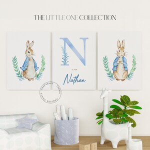 Puede incluir: Tres impresiones de acuarela que representan un conejo azul con una chaqueta azul, una letra N azul con el nombre Nathan y un conejo azul con una chaqueta azul. Las impresiones son sobre fondo blanco y están enmarcadas en un marco blanco.