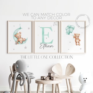 Puede incluir: Tres impresiones enmarcadas con un diseño de acuarela que presenta un osito de peluche, una letra E con el nombre Ethan y un osito de peluche sosteniendo globos. Las impresiones están en una pared blanca con un peluche de pulpo gris, un taburete de madera y una silla de madera con un peluche de oso blanco.
