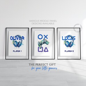 Op de afbeelding: Drie ingelijste prints met een gamingthema. De linker print heeft een blauw aquarelontwerp van een koptelefoon met de naam "Oliver" en de tekst "Player 1". De middelste print heeft een blauw aquarelontwerp van een videogamecontroller met de letters "OX" en de symbolen "□△". De rechter print heeft een blauw aquarelontwerp van een koptelefoon met de naam "Lucas" en de tekst "Player 2".