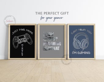 Può includere: Tre stampe incorniciate con testo e grafica a tema gamer. La prima stampa ha uno sfondo nero con un contorno argentato di un controller per videogiochi e il testo "Just Five More Minutes". La seconda stampa ha uno sfondo grigio con un contorno argentato di una lista di controllo con il testo "Eat Sleep Gaming Repeat". La terza stampa ha uno sfondo blu con un contorno argentato di cuffie e il testo "Can't Hear You I'm Gaming".