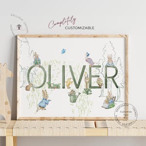 May include: A framed print featuring the name "OLIVER" in green, with watercolor illustrations of rabbits, ducks, and other woodland creatures. The words "Completely Customizable" are above the name. The print has a wooden frame.