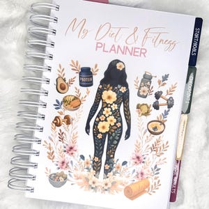 May include: A spiral-bound diet and fitness planner with a floral design. The cover features the text "My Diet & Fitness Planner" and illustrations of food, protein, and exercise equipment. Tabs read "Today", "Start/Goals", "Checkpoint 1", and "Final Results".