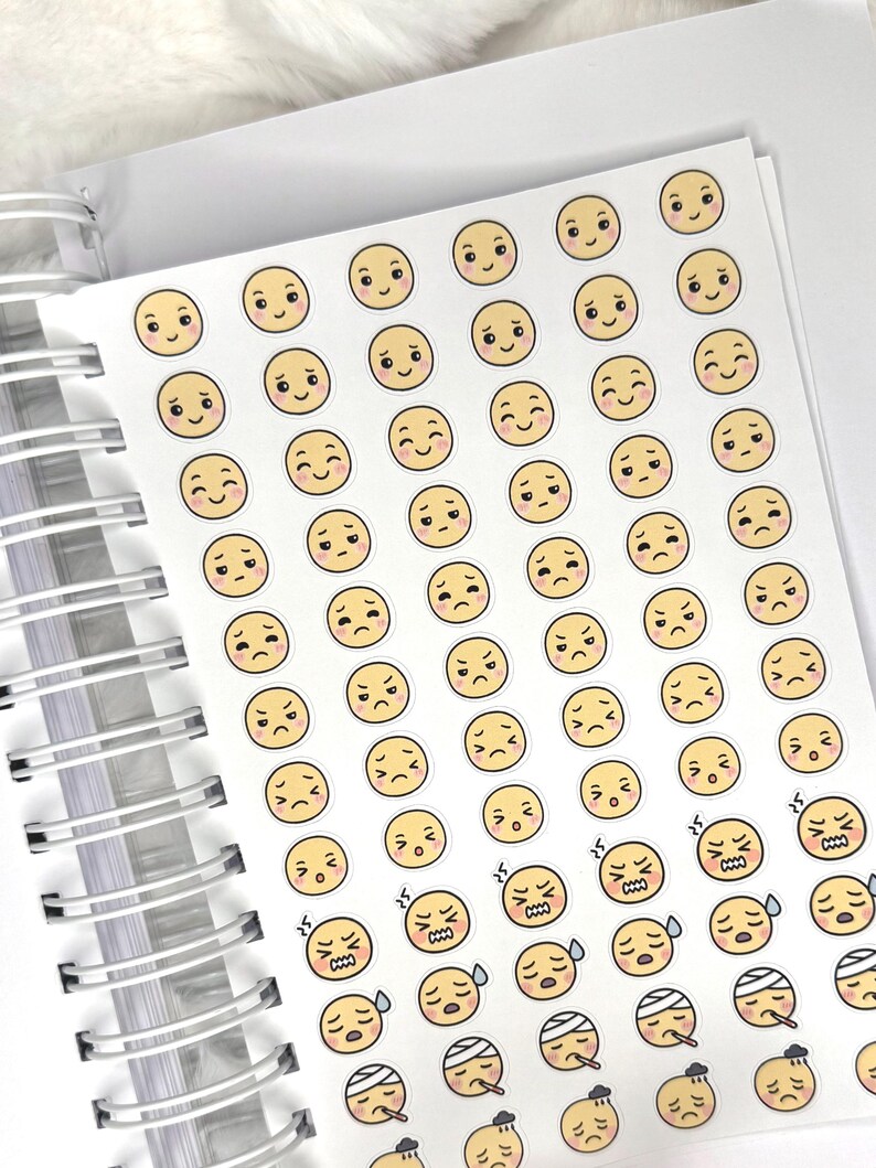 May include: A sheet of stickers featuring various emoji faces with different expressions. The emojis are yellow with black eyes and mouths, depicting emotions from happy to sad, angry, and sick. The stickers are on a white sheet, with a spiral notebook binding visible.