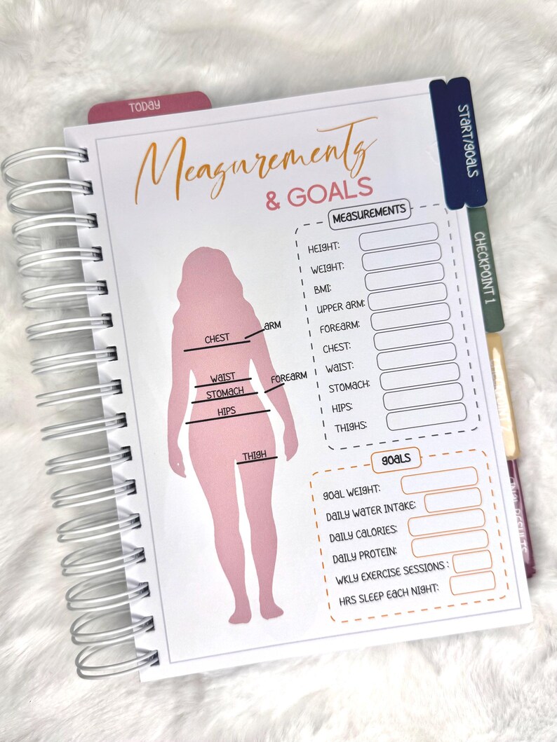 May include: A spiral-bound planner with a pink silhouette and the words "Measurements & Goals." The planner includes sections for recording body measurements and goals, with tabs labeled "Today" and "Start/Goals."