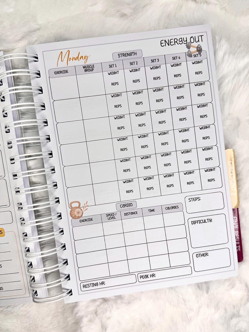 May include: Open spiral-bound fitness planner with a white interior. The planner features sections for strength training, cardio, and steps, with spaces to record exercises, weight, reps, and other metrics. The word "Monday" is written at the top.