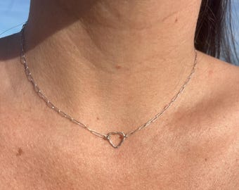 May include: A delicate silver necklace featuring a small, open heart pendant. The necklace has a fine chain with a simple, elegant design. The heart pendant is centered, creating a minimalist and romantic aesthetic.
