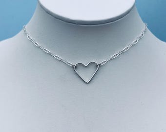 May include: A silver-colored necklace with a heart pendant. The necklace features a delicate chain with oval links. The heart pendant is a simple, open design. The necklace is displayed on a white mannequin against a light blue background.