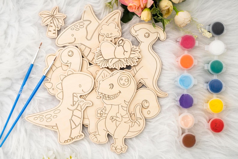 May include: Wooden dinosaur cutouts with paint pots and paintbrushes. The set includes various dinosaur shapes, such as a T-Rex, a Brontosaurus, and a Pterodactyl. The paint pots contain a variety of colors, including red, blue, and green.