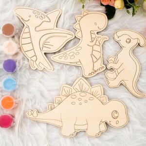 May include: Wooden dinosaur cutouts for painting, including a Pterodactyl, T-Rex, and Stegosaurus. Paint pots with various colors and paintbrushes are included, perfect for a fun craft project. The dinosaurs are approximately 10 inches in length.