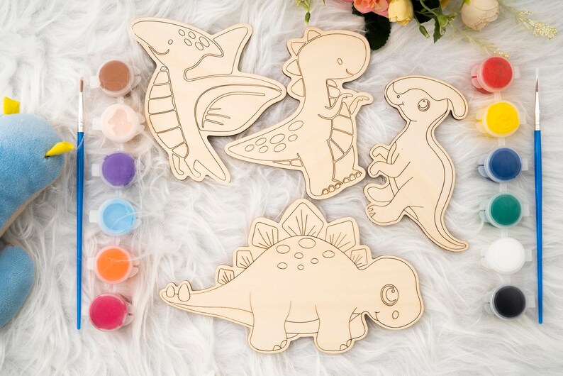 May include: Wooden dinosaur cutouts for painting, including a Pterodactyl, T-Rex, and Stegosaurus. Paint pots with various colors and paintbrushes are included, perfect for a fun craft project. The dinosaurs are approximately 10 inches in length.