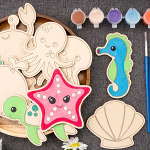 May include: A set of wooden sea creature shapes for painting. The set includes a crab, octopus, jellyfish, whale, turtle, starfish, and seashell. The shapes are unpainted and ready to be decorated with acrylic paints. The set also includes two paintbrushes and a variety of paint colors.