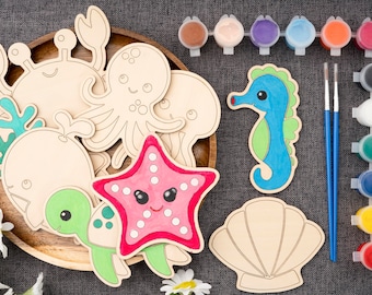 May include: A set of wooden sea creature shapes for painting. The set includes a crab, octopus, jellyfish, whale, turtle, starfish, and seashell. The shapes are unpainted and ready to be decorated with acrylic paints. The set also includes two paintbrushes and a variety of paint colors.